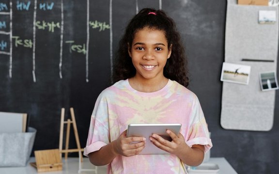 Ein Mädchen steht mit einem Tablet in der Hand vor einer Tafel