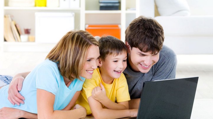 Frau, Kind und Mann blicken gemeinsam in einen Laptop und lachen