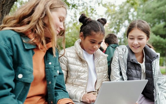 Kinderschutz auf digitalen Geräten Drei Kinder, die in der Natur vor einem Laptop sitzen.