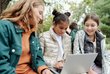 Kinderschutz auf digitalen Geräten Drei Kinder, die in der Natur vor einem Laptop sitzen.