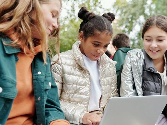 Kinderschutz auf digitalen Geräten Drei Kinder, die in der Natur vor einem Laptop sitzen.