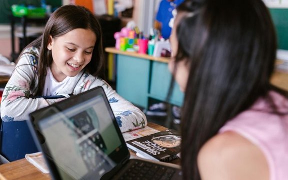 Zwei Schülerinnen in einem Klassenzimmer und einem Laptop